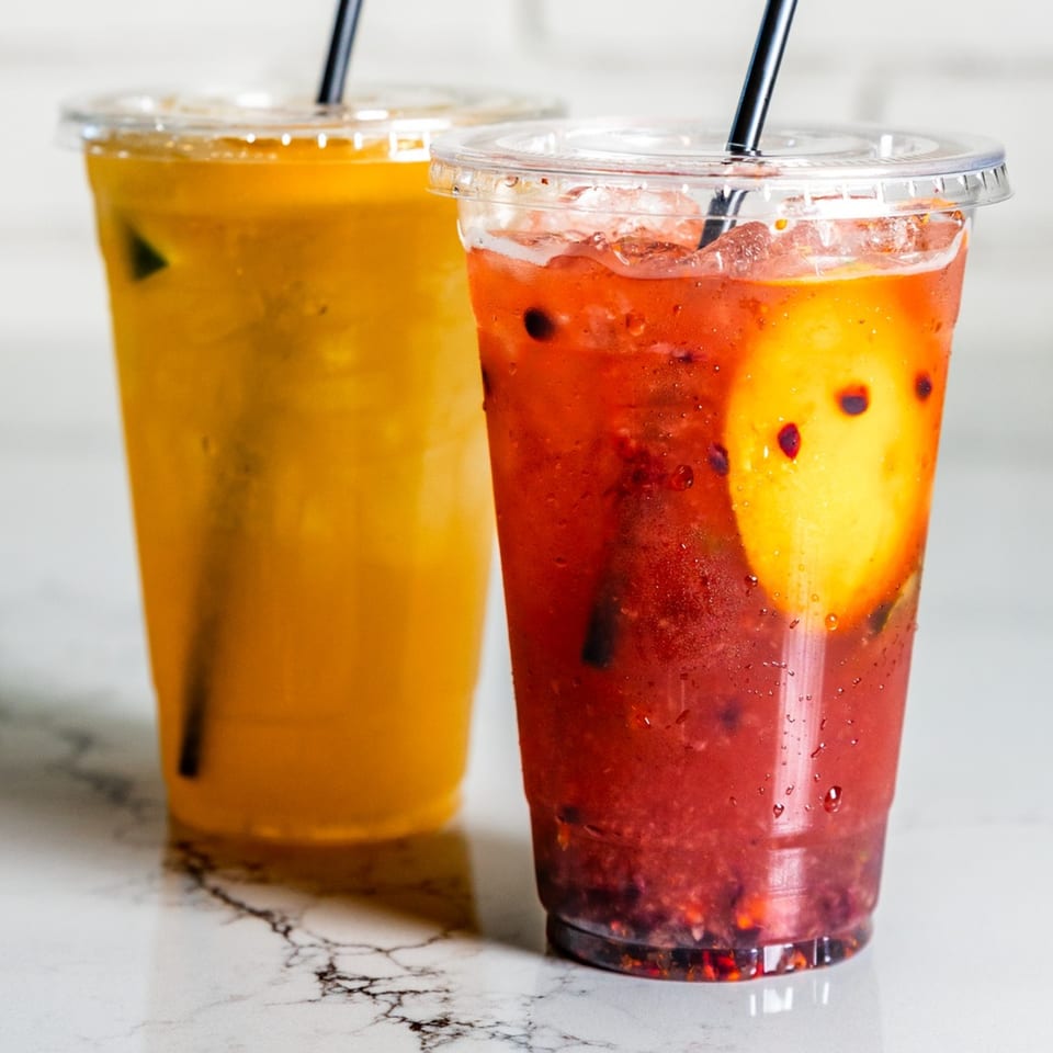 Two vibrant Federales Street Tacos drinks, one yellow and one red with fruit, on a marble surface.