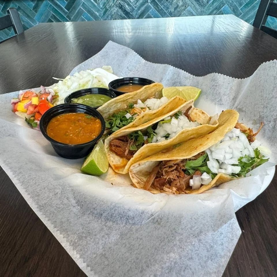 Three Federales Street Tacos with various fillings, lime wedges, and dipping sauces on a white paper-lined tray.