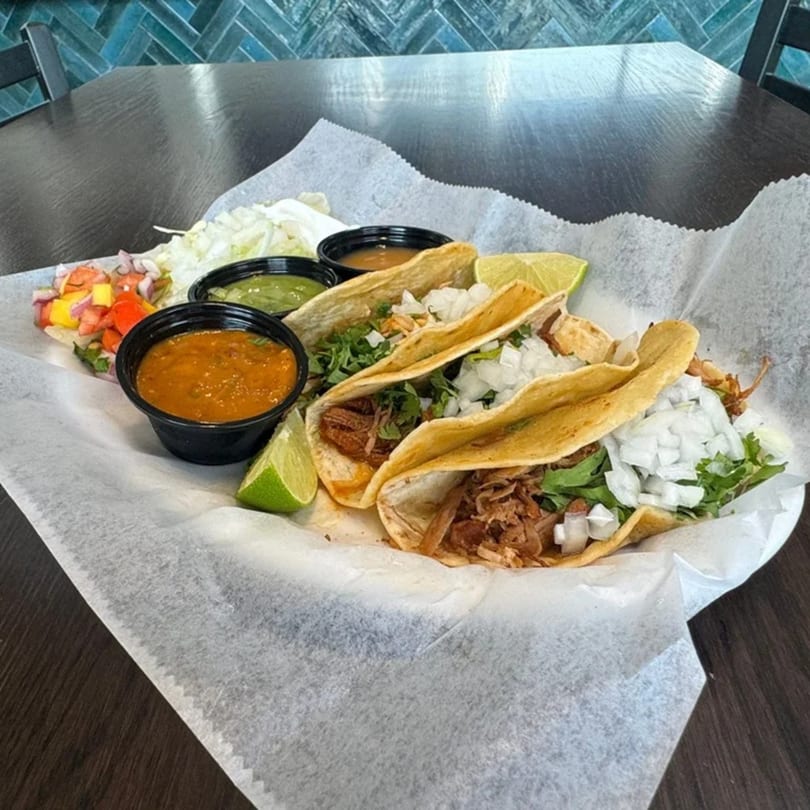 Three Federales Street Tacos with various fillings, lime wedges, and dipping sauces on a white paper-lined tray.