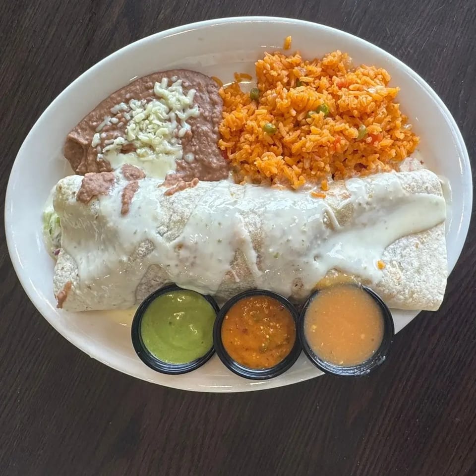A Federales Street Tacos burrito covered in white sauce, with rice, refried beans, and three dipping sauces.