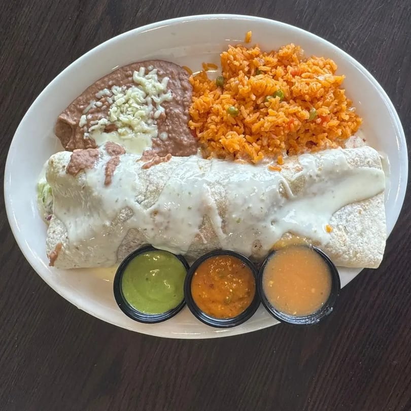 A Federales Street Tacos burrito covered in white sauce, with rice, refried beans, and three dipping sauces.